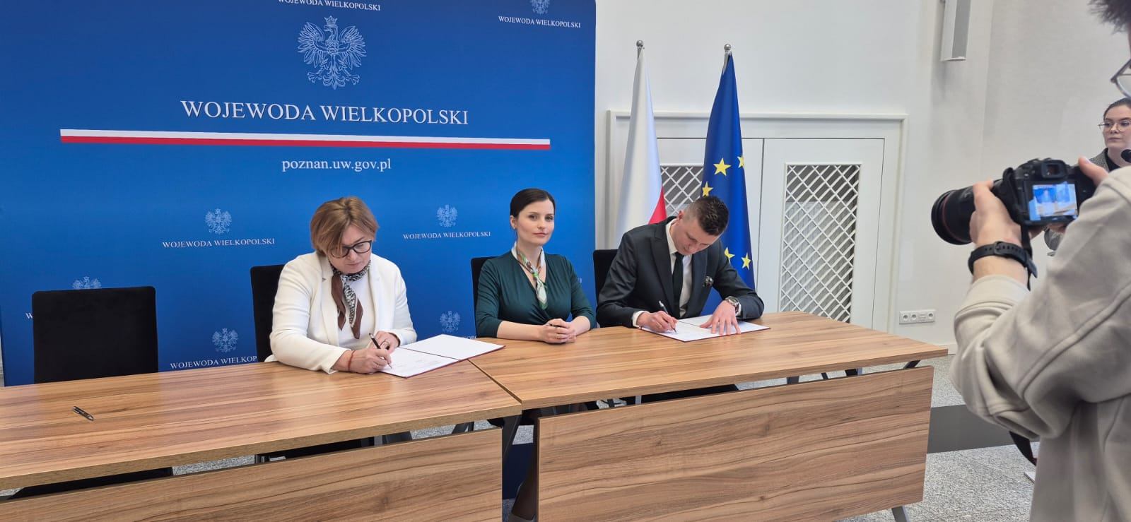 na zdjęciu widoczne są trzy osoby, skarbnik gminy, wojewoda wielkopolski oraz wójt gminyosoby te podpisuja umowe