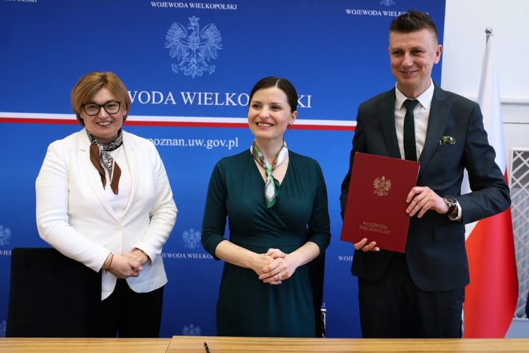 na zdjęciu widoczne są trzy osoby, skarbnik gminy, wojewoda wielkopolski oraz wójt gminy, ktory trzyma w reku teczke z podpisana umowa na przebudowe drogi